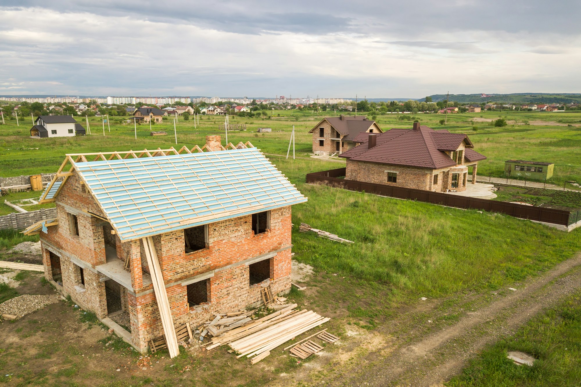 Aerial view of a brick house with wooden roof frame under construction.