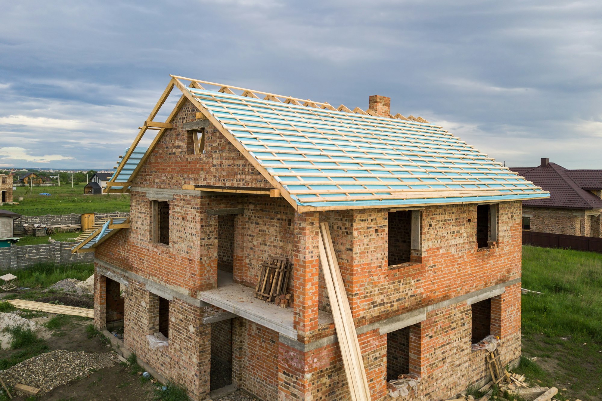 Aerial view of a brick house with wooden roof frame under construction.