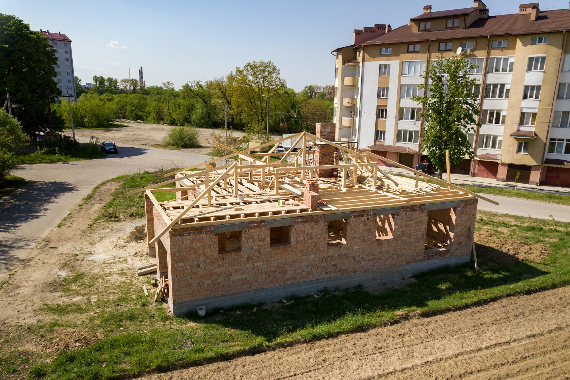 Aerial view of unfinished brick house with wooden roof frame structure under construction