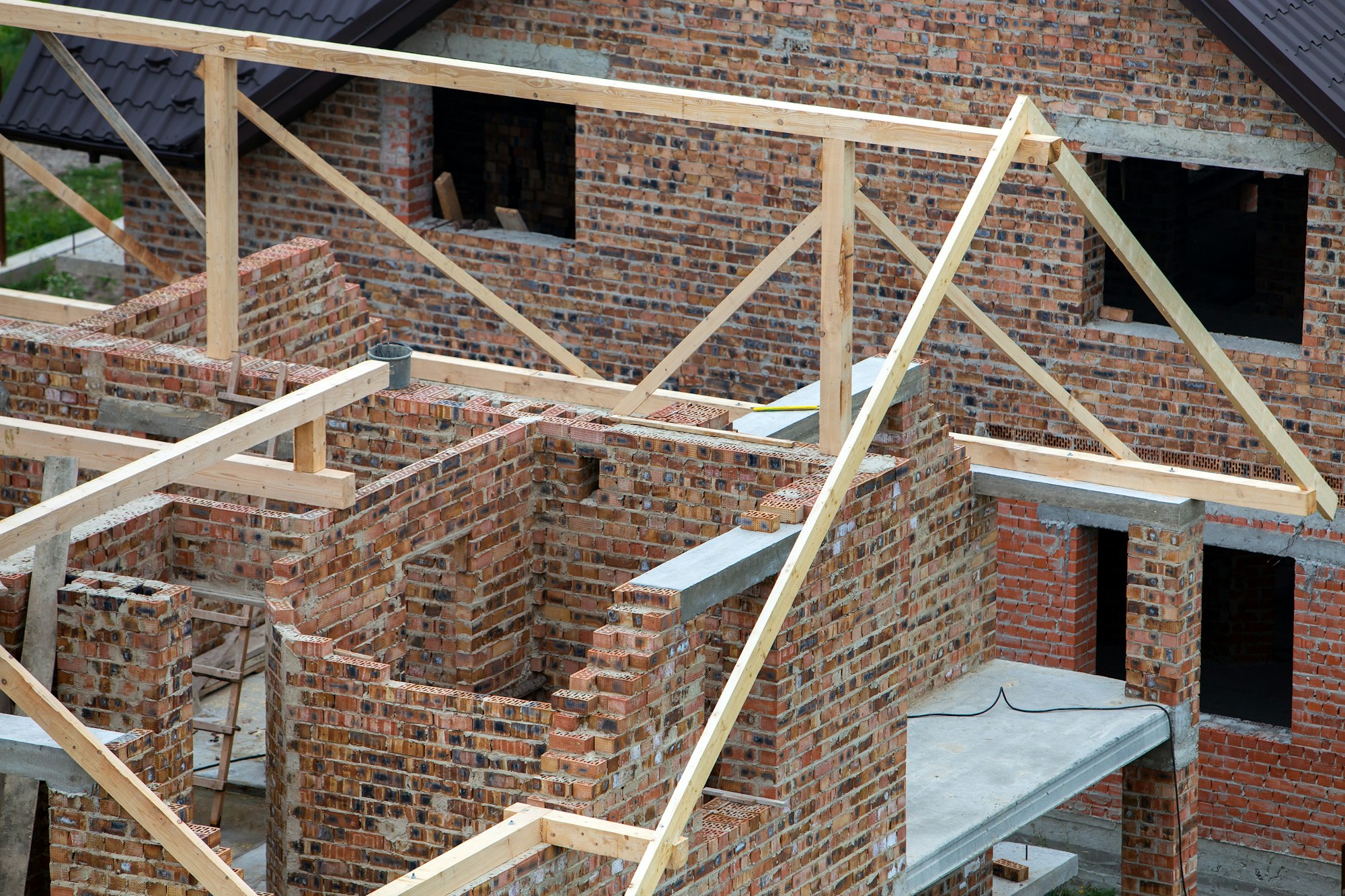 Unfinished brick house with wooden roof structure under construction.